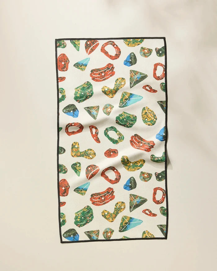 The Geometry Boulder Landscape fitness towel features colorful abstract gemstone shapes in red, green, yellow, and blue on cream with a black border. Made from ultra-absorbent recycled materials, the rectangular cloth is shown laid flat with slight wrinkles.