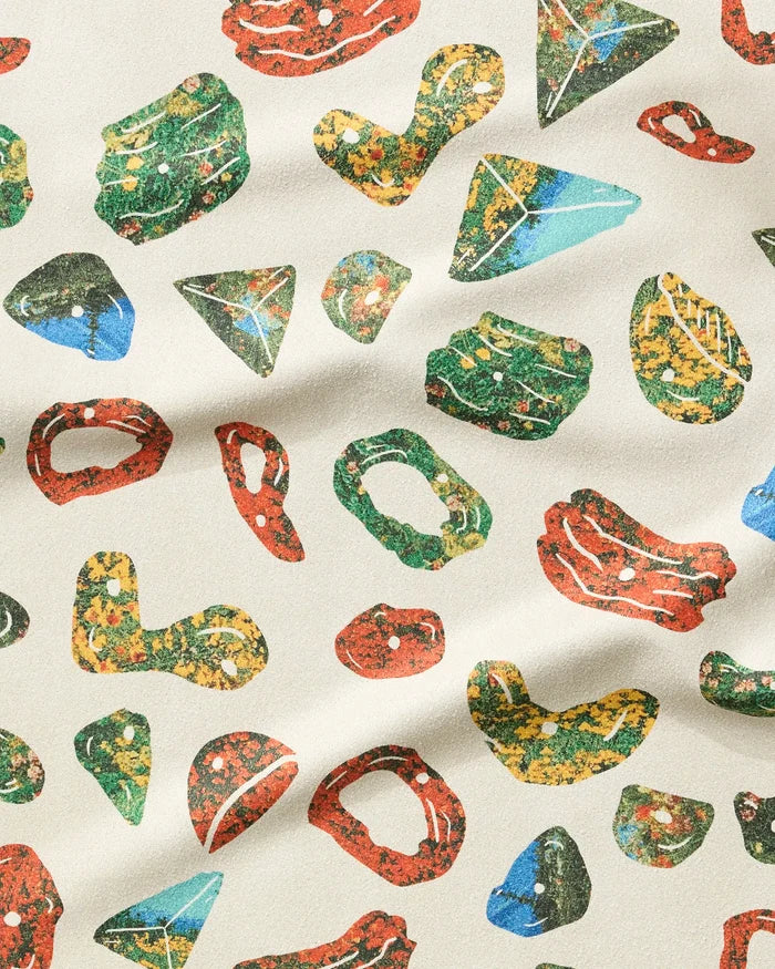 The Boulder Landscape fitness towel by Geometry is cream-colored and ultra-absorbent, featuring colorful, climbing hold-inspired shapes in red, yellow, green, and blue scattered randomly across the surface.