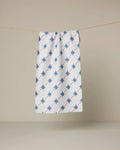 The Estrella Norte towel by Geometry, featuring blue eight-pointed stars in diagonal lines on a white background, hangs on a clothesline against plain beige.