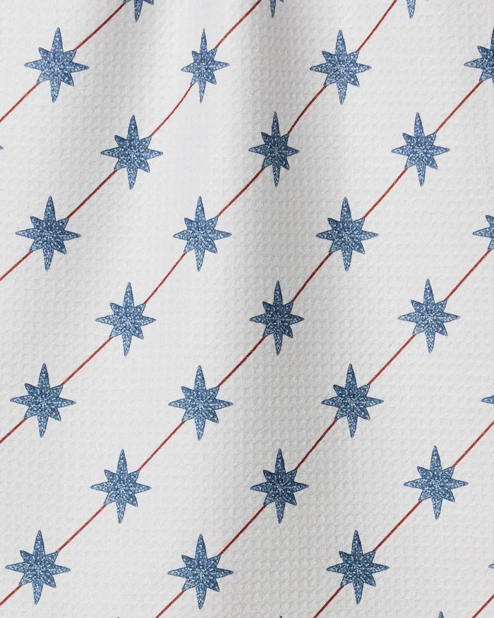 The Estrella Norte towel by Geometry is white and quick-drying, featuring a textured surface with blue eight-pointed stars in diagonal rows, intersected by thin red diagonal lines.