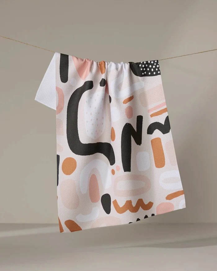 Fall Geometry" by Marina Solodka is a tea towel with abstract black, peach, and beige shapes, crafted from recycled materials and displayed against a neutral background.