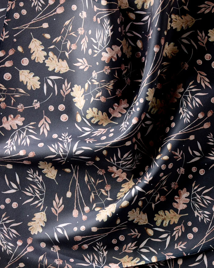 Fallen Oak by Katie O'Shea is a dark, silky napkin made from recycled fabric, featuring a pattern of light leaves, branches, and berries that catches the light to reveal its beautifully smooth texture.