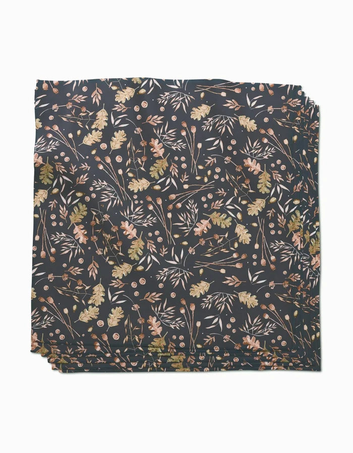 A stack of Fallen Oak Geosuede fabric by Katie OShea, featuring a delicate leaf, branch, and flower pattern in earthy pink, gold, and green tones on a dark background—crafted from post-consumer recycled materials.