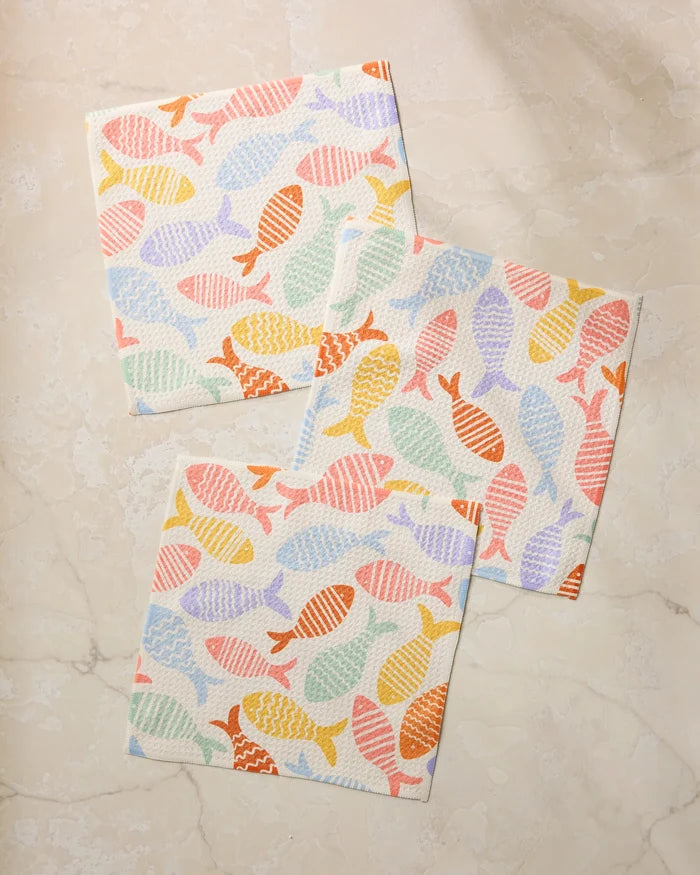 The Geometry Fish Flip set features three super-absorbent square dishcloths in pastel fish patterns, made from recycled materials and shown on a light marble surface.