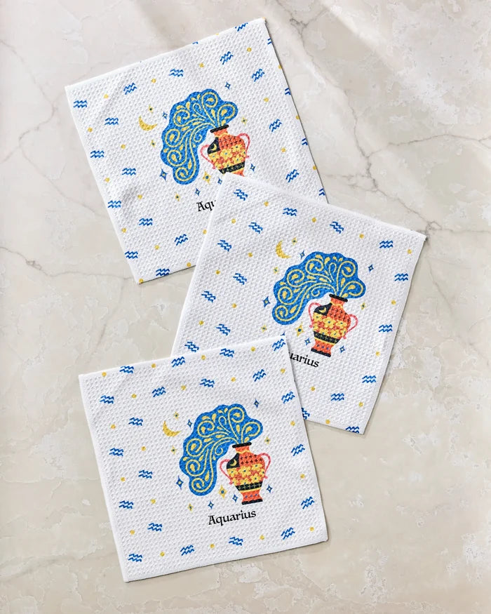 Three "Free Aquarius" paper napkins by Heather Zhou, featuring a colorful Aquarius zodiac design with a water jug and blue waves, made from recycled materials and arranged on a light marble surface.