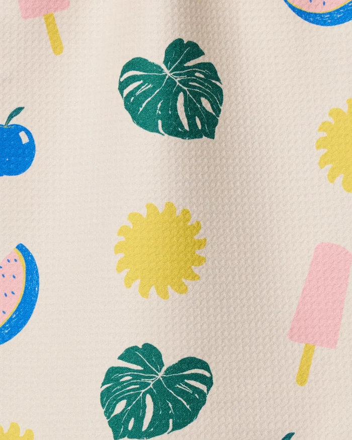 Geometry’s Fruity Pop kitchen towel features green monstera leaves, yellow flowers, blue cherries, pink popsicles, and a pink-and-blue watermelon slice on a light background—ultra-absorbent and made from recycled materials.