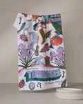 The Geometry "Greetings From Tennessee" tea towel, featuring vibrant state icons and phrases, hangs on a line above plates resting on the table.