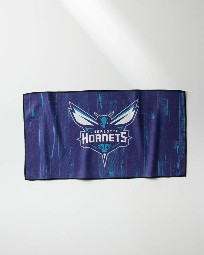 The Hornets Zone fitness towel by NBALAB x Geometry features the Charlotte Hornets logo and team name in white and teal on a blue, wood-textured background. This quick-drying rectangular workout towel displays a stylized hornet design.