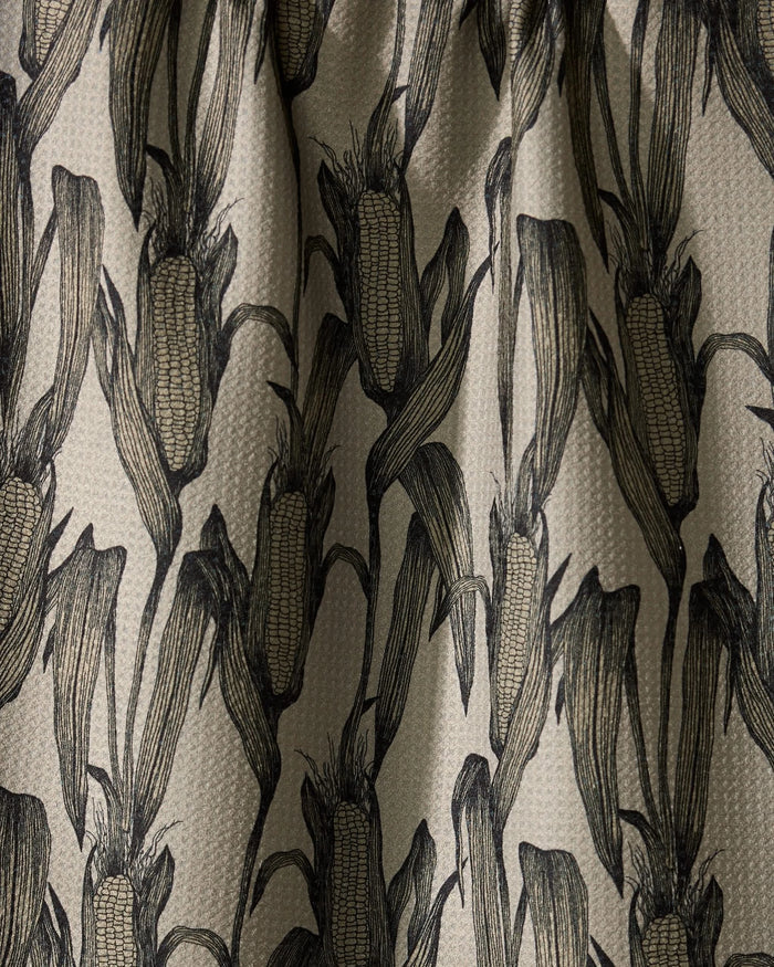 A close-up of Geometrys Husk fabric, featuring black line-drawn corn-on-the-cob motifs on beige—ideal as a stylish kitchen tea towel with its textured, repeating pattern.