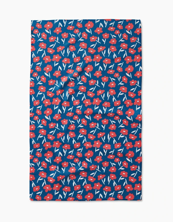 The Luca Daisy Red tea towel by Hufton Studio features a blue background with small red flowers, white accents, and green stems in a repeating pattern, made from recycled materials.