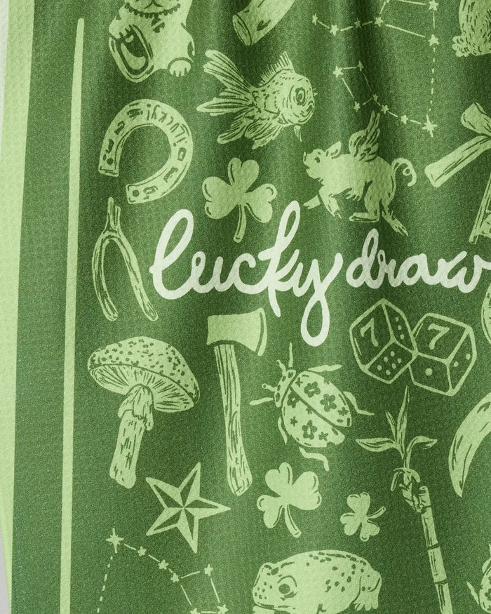 The Lucky Draw tea towel by Geometry features green eco-friendly fabric with white lucky symbols—horseshoe, four-leaf clover, pig, wishbone—and "Lucky draw" in script. Perfect as a reusable kitchen towel.