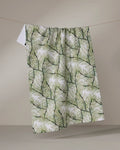 The Geometry Pinewell recycled kitchen towel, featuring a green pine needle pattern, hangs naturally on a line against a beige background, highlighting its bold botanical design.