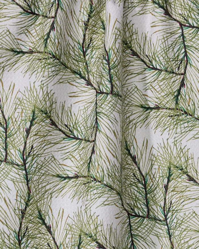 A close-up of Geometry's Pinewell towel showcases its ultra-absorbent fabric, featuring a festive pattern of overlapping green pine needles on a white background with gentle folds for a natural look.