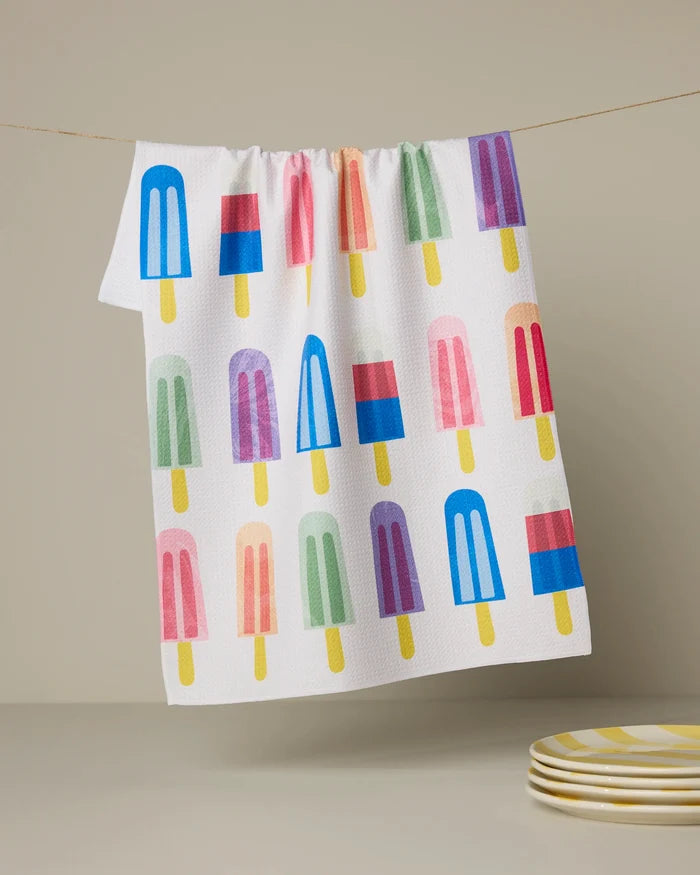 The Poppy Popsicles tea towel by Geometry features playful popsicle illustrations on white and hangs above a stack of yellow and white striped plates—perfect for adding a cheerful touch to your kitchen.