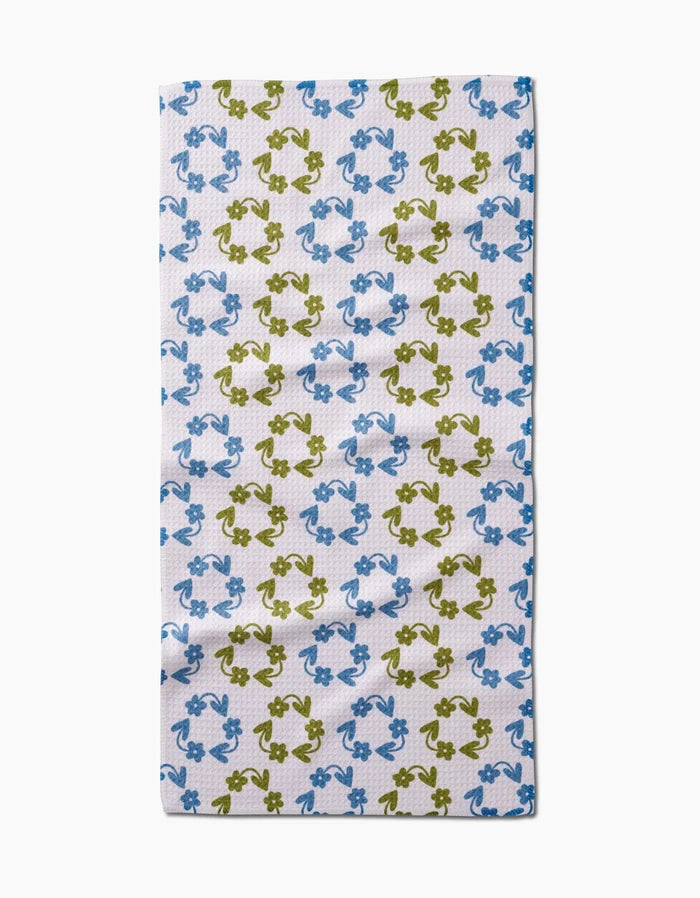 The Kayla Ann Recycled Floral Bar Towel is rectangular and ultra-absorbent, featuring a repeating pattern of blue and green frogs in alternating rows. Made from post-consumer recycled materials, it’s displayed flat on a plain white background.