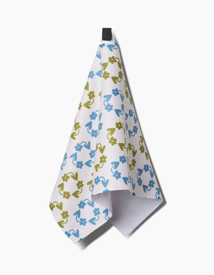 The Kayla Ann Recycled Floral bar towel features blue and green flowers on white, hanging from a black loop. Made from ultra-absorbent, post-consumer recycled materials, its a stylish and eco-friendly choice for your home.