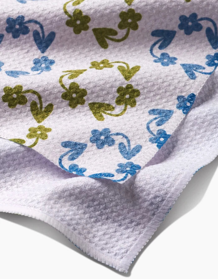 A close-up of the Kayla Ann Recycled Floral Bar Towel, featuring ultra-absorbent white fabric with soft blue and green floral and heart patterns arranged decoratively in a repeating design.