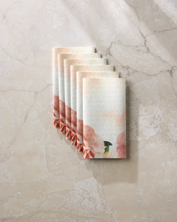Six folded Rhapsody in Bloom paper towels by Stefanie Bales, featuring a soft pink floral pattern and a small green bird, are arranged neatly on a light marble surface.
