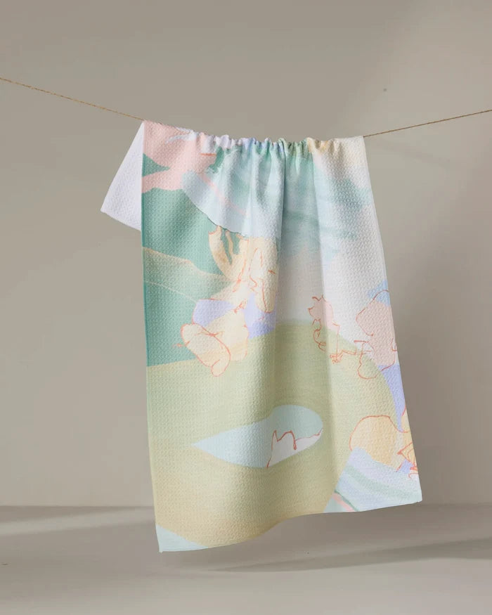 The Secret Fort dish towel by Kristina Baker, featuring pastel hues and abstract, playful animal and shape designs, hangs from a clothesline against a neutral background.
