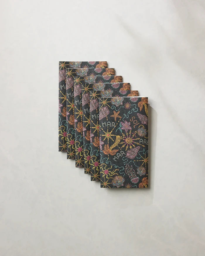 Six Sol Mar Black notebooks by Geometry, featuring vibrant marine-themed patterns, are arranged fan-style on a marble surface—an inspiring look for eco-friendly kitchen towels.