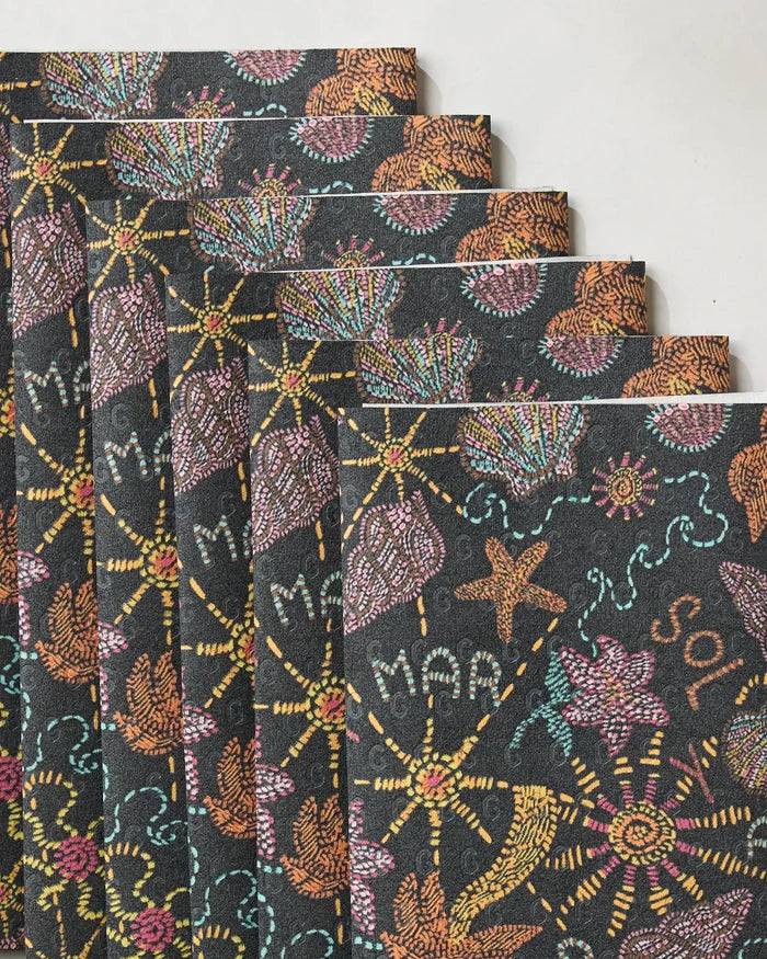 Several Geometry Sol Mar Black notebooks with dark covers and intricate, colorful patterns are fanned out on a light surface next to eco-friendly kitchen towels, creating a stylish and sustainable workspace vibe.