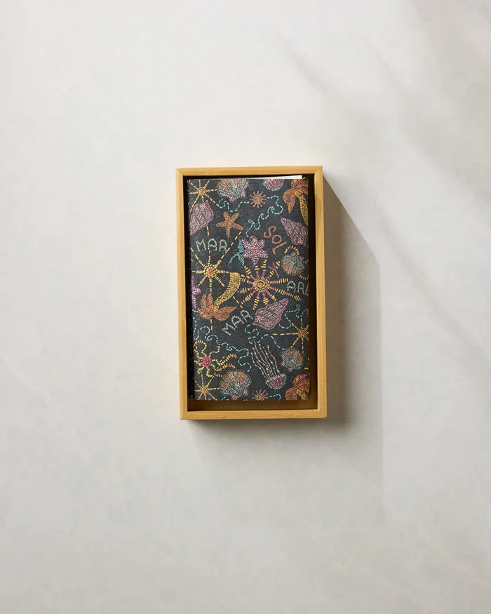 The Sol Mar Black by Geometry is a rectangular black scarf with embroidered sea creatures and MARA text, neatly folded in a wooden box—an ideal sustainable accent when paired with eco-friendly kitchen towels.