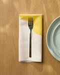 A Solar Light by Geometry sits on a light wooden table next to a pale green plate, adding a modern, eco-friendly touch to your table setting.