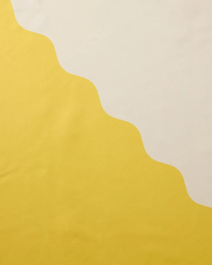 A wavy, scalloped line divides a yellow area and a cream-colored area, forming a simple abstract pattern inspired by recycled dinner napkins on Geometry’s Solar Light.