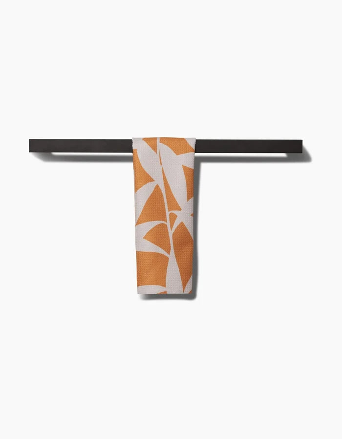 The PrintedPlant Solidago bar towel, crafted from recycled materials with an orange abstract leaf pattern, is neatly draped over a black horizontal towel bar against a plain white background.