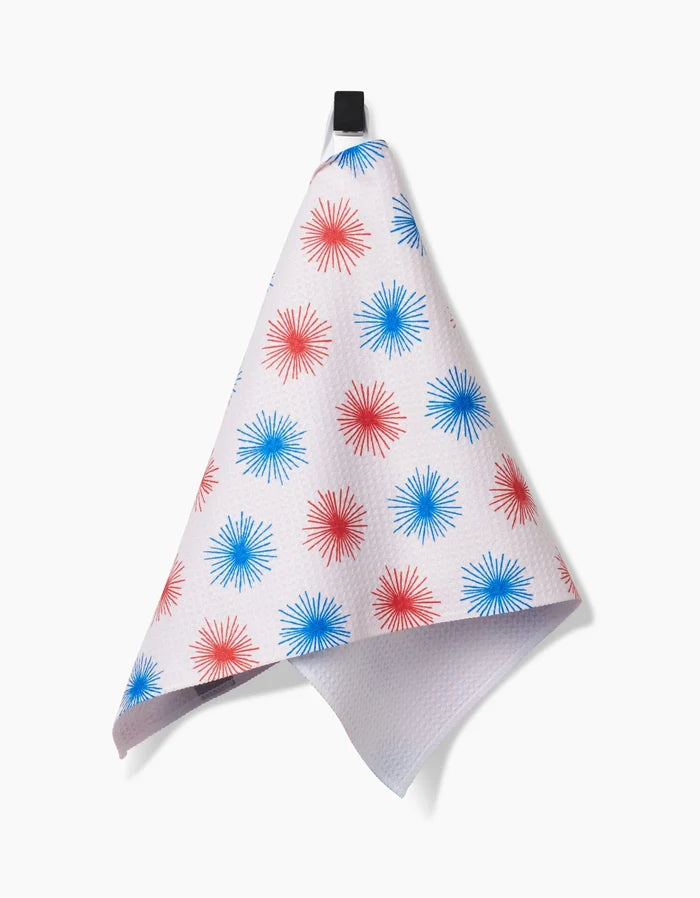 The Kayla Ann Sparkler Splash Bar Towel, made from Geoweave fabric with red and blue starburst patterns, hangs by a black loop against a plain white background.
