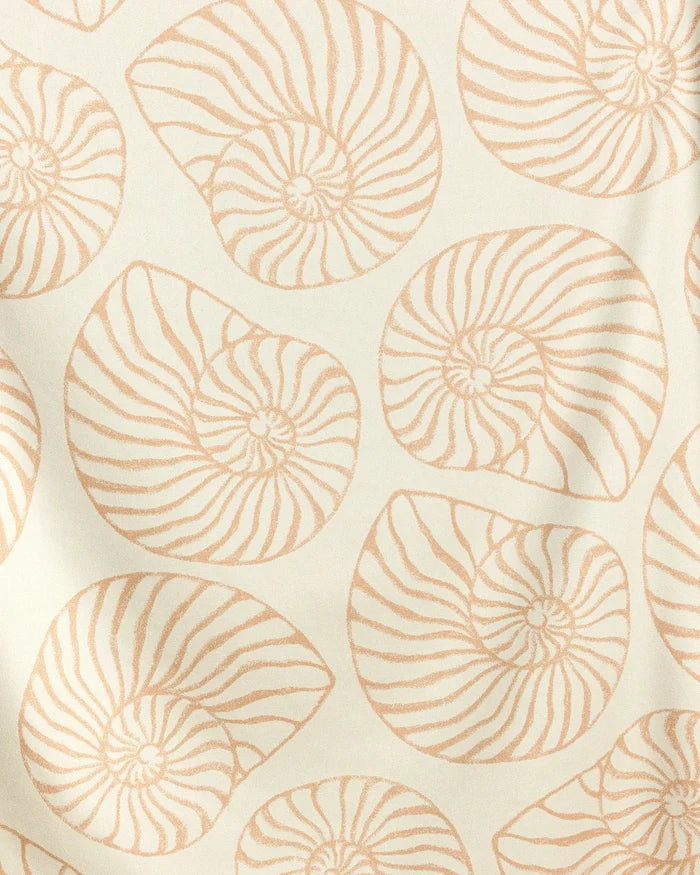 Spira by Geometry features quick-drying fabric with a repeating pattern of beige nautilus shells on an off-white background. The sea-inspired design is perfect for use as a stylish beach blanket.