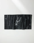 The Spurs Zone towel by NBALAB x Geometry is a black rectangular fitness cloth with a subtle wood grain pattern and a white and silver San Antonio Spurs logo at the center, perfect for fans and athletes.