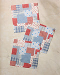 The Geometry Stars and Stitches set includes three square fabric napkins with a red, white, and blue patchwork of stars, checks, and stripes—perfect for adding festive flair to your kitchen.