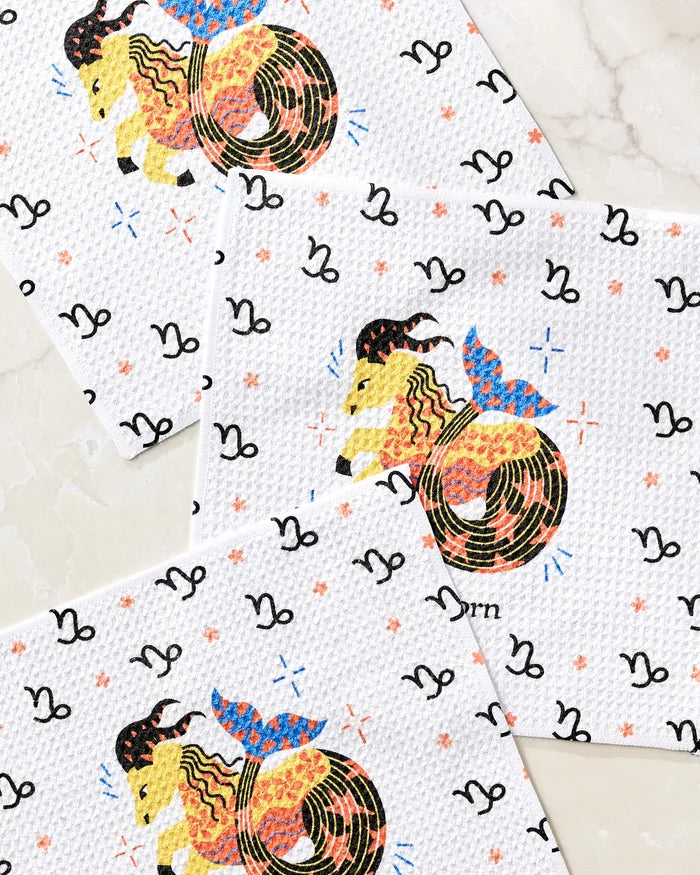 The Steadfast Capricorn dishcloth set by Heather Zhou includes three recycled towels with Capricorn goat-fish symbols, colorful stars, and black zodiac motifs—perfect for any zodiac fan's kitchen.