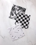 Three super-absorbent GEOMETRY "The Best" dishtowels rest on white marble: one has a black floral design, another a buffalo check with hearts, and the third features scattered text and tiny hearts—all made from recycled materials.