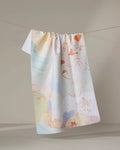 The "Tree House" kitchen towel by Kristina Baker, featuring pastel colors and abstract, line-drawn faces and hands, hangs on a thin string against a neutral background. Ultra-absorbent and stylish for any kitchen.