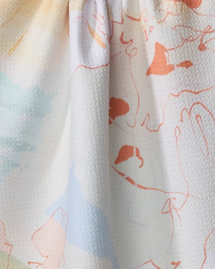 A close-up of Tree House, an ultra-absorbent kitchen towel by Kristina Baker, showing textured white fabric with pastel and orange abstract line drawings—possibly faces and hands—scattered across its surface.