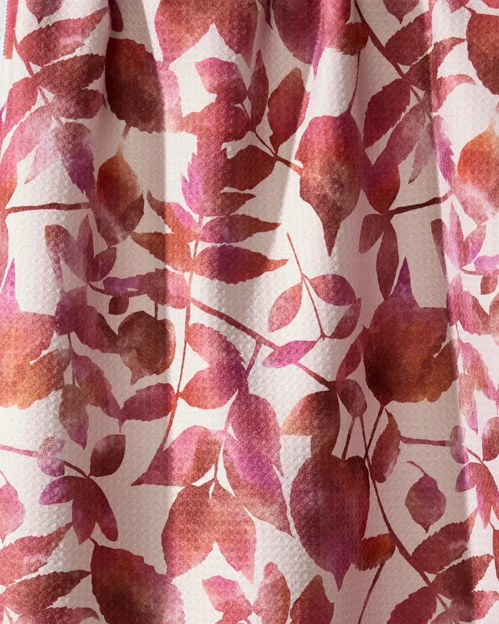 A close-up of Geometry’s Watercolor Dreaming tea towel, made from recycled materials, shows its pink, red, and brown leaf and flower pattern on a light background with a charmingly textured fabric.
