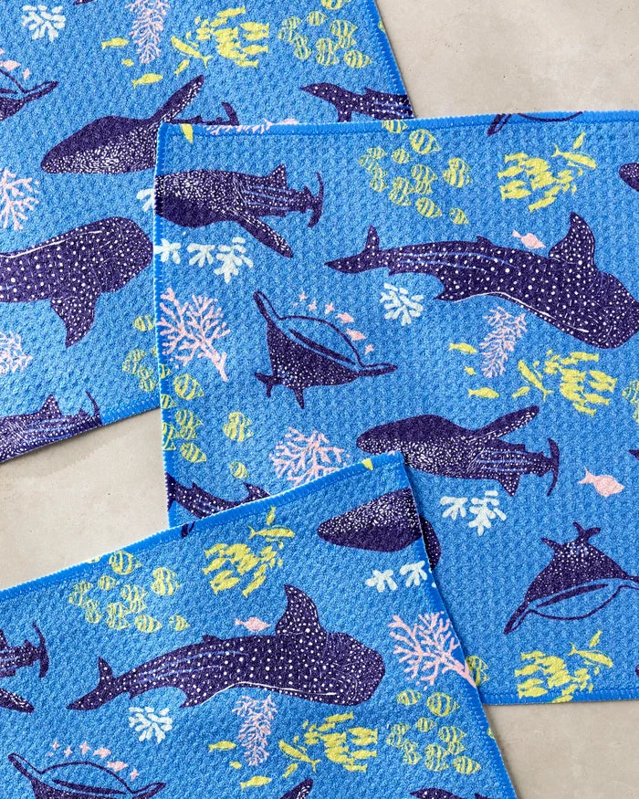 The Elisabeth Wing Whale Shark dishcloth set includes three blue, recycled dishcloths with whale shark, coral, and colorful fish illustrations in an overlapping pattern on a light surface.