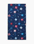 The Whirlwind Pins bar towel by Rebecca Bobko is navy blue, made from recycled materials, and features a festive pattern of red, white, and blue pinwheels with small white stars.