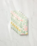 Six folded Wildflowers in Bloom reusable paper towels by Jasmine Blooms Designs, featuring pastel pink, yellow, and green floral patterns, are neatly arranged in an overlapping row on a white marble surface.