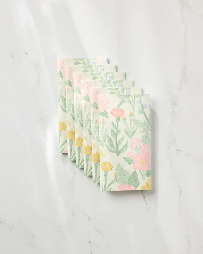Six folded Wildflowers in Bloom reusable paper towels by Jasmine Blooms Designs, featuring pastel pink, yellow, and green floral patterns, are neatly arranged in an overlapping row on a white marble surface.