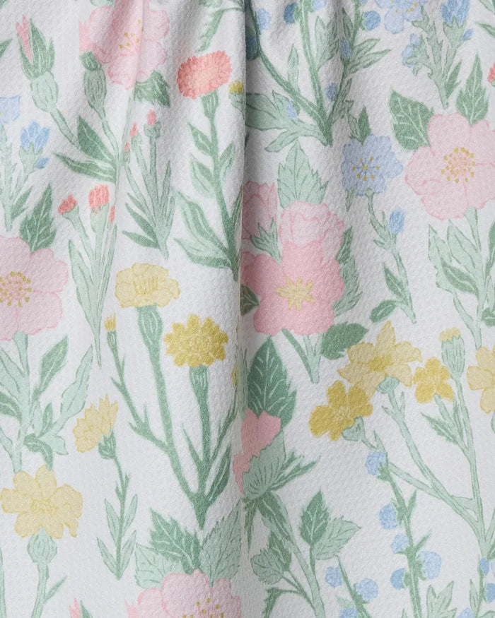 A close-up of the Wildflowers in Bloom kitchen towel by Jasmine Blooms Designs, made from recycled materials with a textured white fabric featuring pastel pink, yellow, and blue flowers with green leaves.