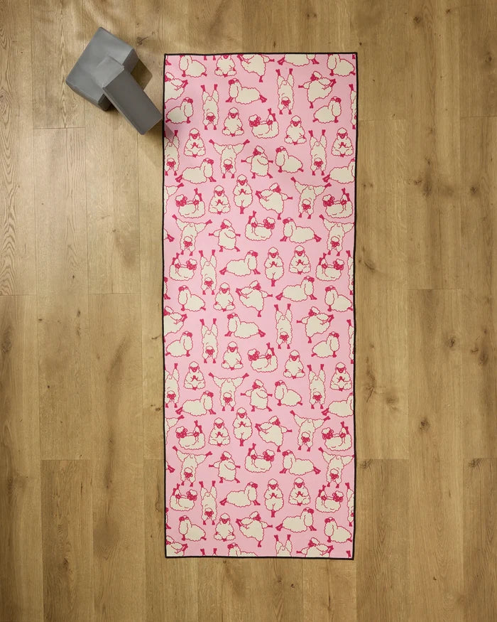 The Geometry Yoga Sheep mat features playful sheep poses on pink, resting on wood with a gray yoga block and recycled towel for extra comfort and eco-friendly support.